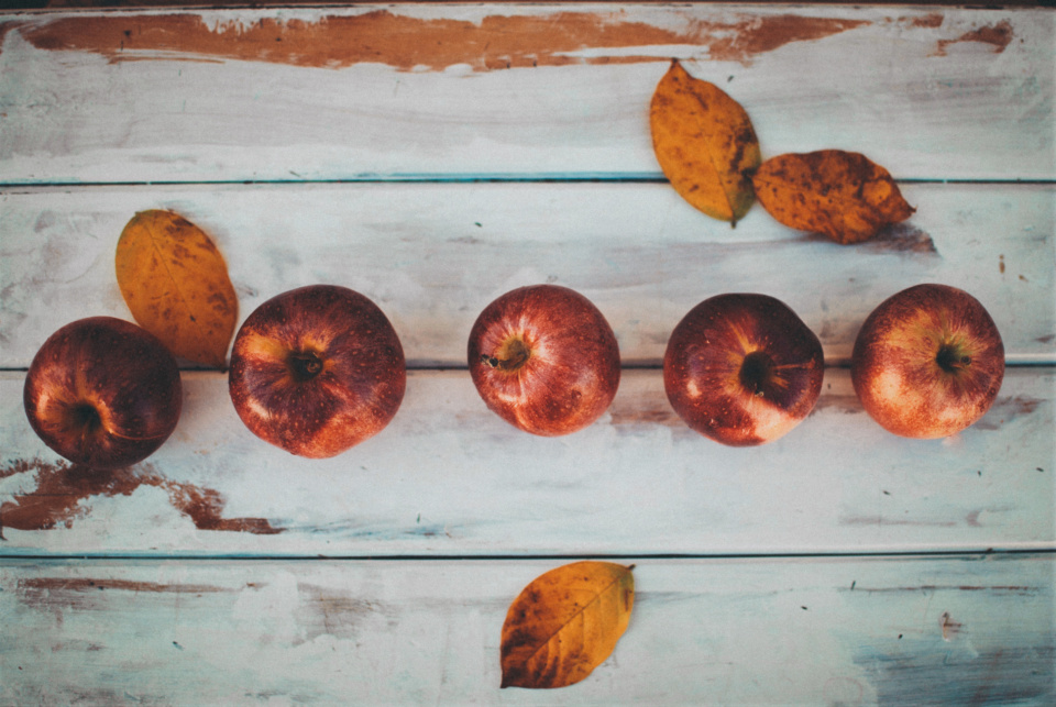 Red apples and yellow fall leaves on white wooden background